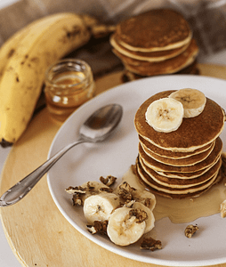A stack of pancakes topped with banana slices and drizzled with syrup on a plate.